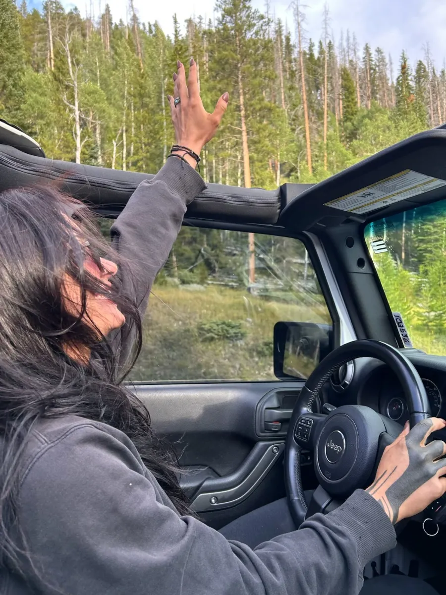 Solo traveler driving through the forest with hand raised