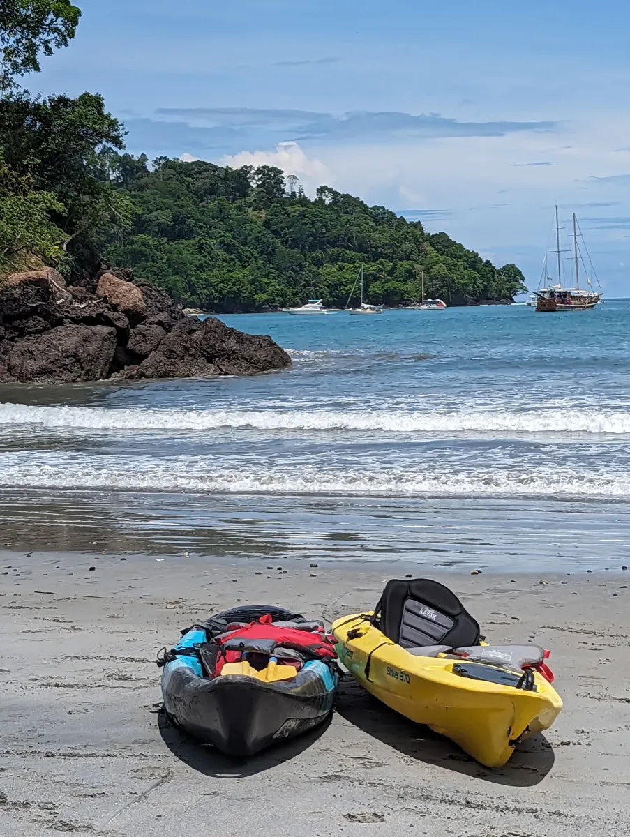Kayaks on a tropical beach with sailboats in the bay